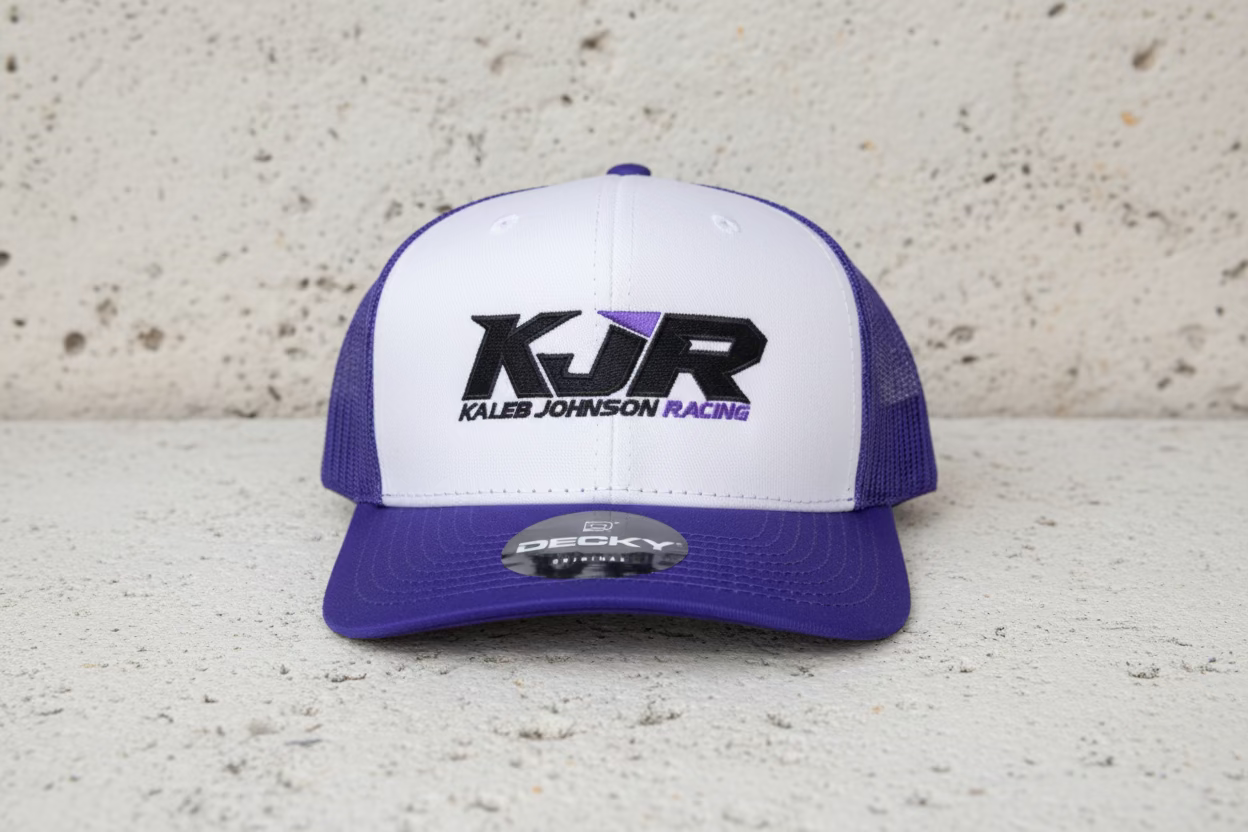White and purple trucker hat with KJR logo on a textured surface